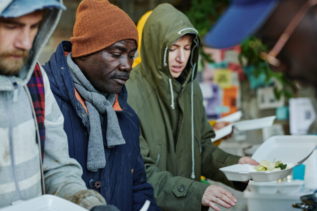 Group of homeless people in warm clothing coming to eat free food giving by volunteers from charity community
