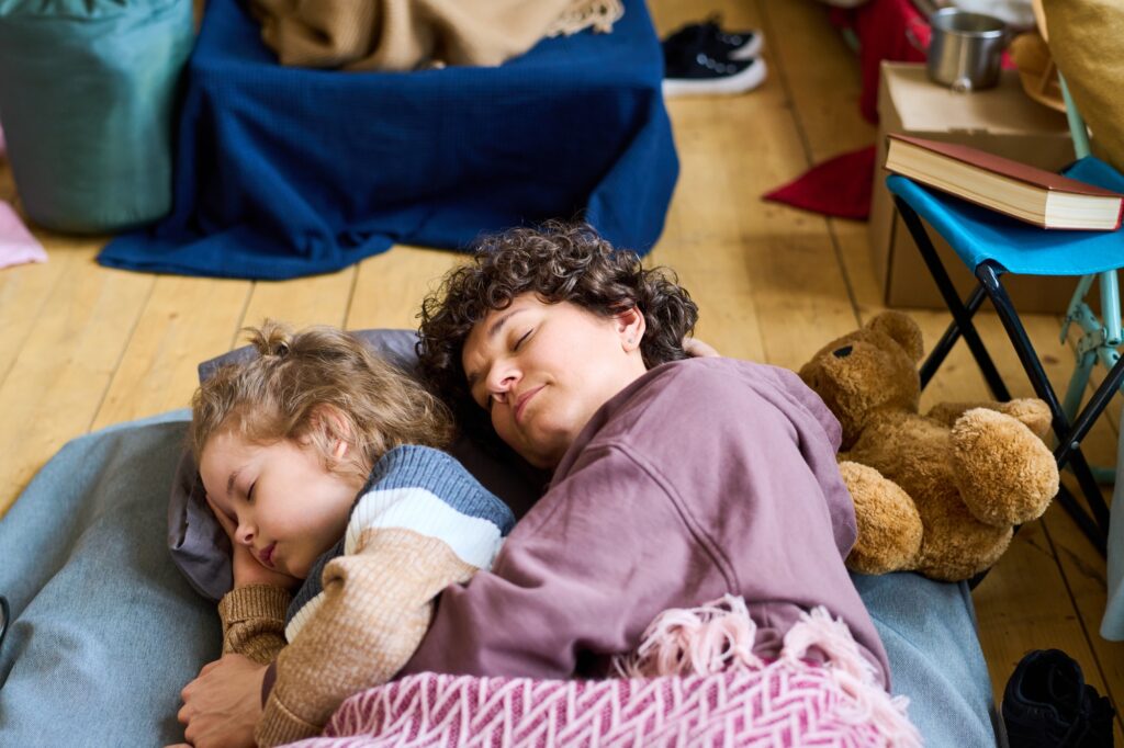 Adorable boy with blond curlt hair and his mother sleeping on the floor