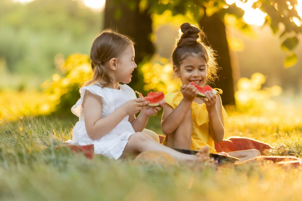 Two kids eating of watermelon in the garden. Kids eat fruit outdoors. Healthy snack for children.